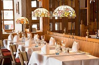 Eingedeckte Tische im Restaurant Adlerstube des Sunstar Hotels Grindelwald mit Tiffany-Lampen und Holzvertäfelung