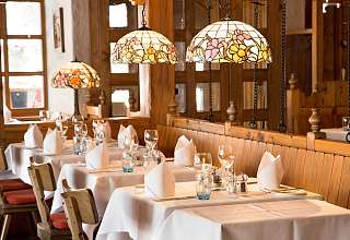 Eingedeckte Tische im Restaurant Adlerstube des Sunstar Hotels Grindelwald mit Tiffany-Lampen und Holzvertäfelung