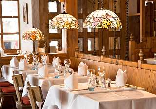 Rustic interior of the Adlerstube featuring wood panelling, decorative pendant lights and a wine barrel – traditional Tyrolean-style ambiance.
