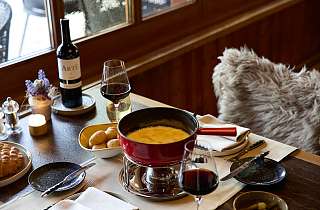 Gedeckter Tisch mit Käsefondue, Brot und Rotwein im Restaurant Adlerstube des Sunstar Hotels Grindelwald