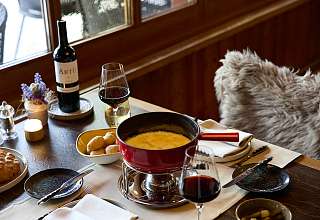 Gedeckter Tisch mit Käsefondue, Brot und Rotwein im Restaurant Adlerstube des Sunstar Hotels Grindelwald