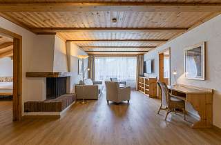 Wohnbereich der Wetterhorn Suite im Sunstar Hotel Grindelwald mit offenem Cheminée, Sitzecke und Schreibtisch unter Holzbalkendecke