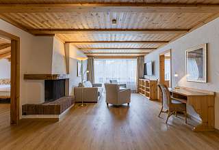 Wohnbereich der Wetterhorn Suite im Sunstar Hotel Grindelwald mit offenem Cheminée, Sitzecke und Schreibtisch unter Holzbalkendecke