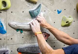 Gros plan sur des mains agrippant des prises d'escalade colorées sur un mur de bloc. © David Birri
