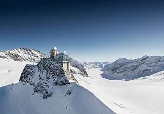 Vue sur l'observatoire du Sphinx sur une crête rocheuse enneigée, entourée par le vaste glacier d'Aletsch et des sommets enneigés. © Jungfraubahnen