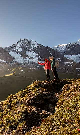 Wanderer auf einem Berggrat oberhalb von Grindelwald mit Blick auf das Dorf und die umliegende Alpenlandschaft