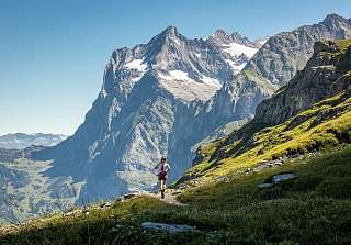 A runner on a mountain trail above Grindelwald with impressive views of the snow-capped peaks of the Bernese Alps – trail running at Sunstar Hotel Grindelwald.