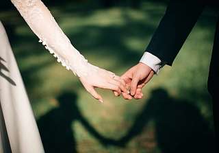 Newlywed couple holding hands outdoors, close-up of hands with wedding rings