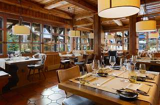 Eingedeckte Tische im Restaurant Adlerstube des Sunstar Hotels Grindelwald mit Holzvertäfelung, Pendelleuchten und Fensterfront zur Dorfstrasse
