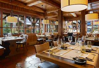 Eingedeckte Tische im Restaurant Adlerstube des Sunstar Hotels Grindelwald mit Holzvertäfelung, Pendelleuchten und Fensterfront zur Dorfstrasse