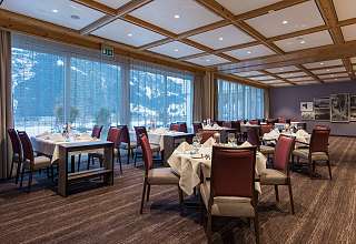 Eingedeckte Tische im Restaurant des Sunstar Hotels Grindelwald mit Panoramafenstern und Blick auf verschneite Berge
