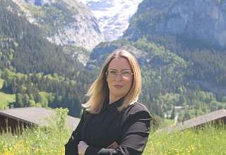 HR Manager Ivana Ladika stands on a green meadow with a mountain panorama in the background