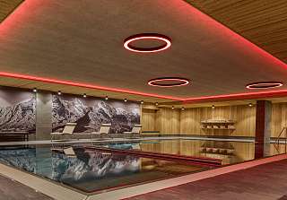 Illuminated indoor pool with wood panelling and loungers, with a large black-and-white image of the Bernese Alps on the wall.