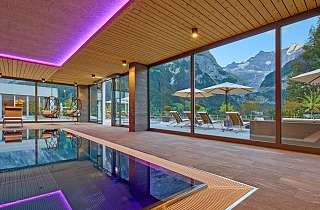 Innenpool im Sunstar Hotel Grindelwald mit violetter Ambientebeleuchtung, Hängesesseln und Panoramafenstern zur Terrasse und Bergkulisse
