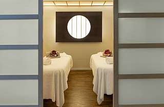Behandlungsraum im Spa des Sunstar Hotels Grindelwald mit zwei Massageliegen und rundem Lichtelement an der Wand