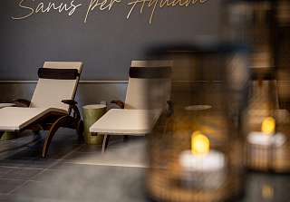 Ruheraum im Sunstar Hotel Grindelwald mit Liegen vor einer Wand mit dem goldenen Schriftzug «Sanus per Aquam», im Vordergrund unscharf zwei Laternen mit Kerzenlicht