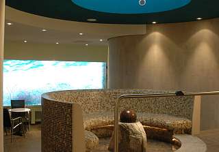 Wellnessbereich des Sunstar Hotel Grindelwald mit Kneippbecken, Kugelbrunnen und geschwungener Mosaikbank, im Hintergrund eine beleuchtete Glaswand