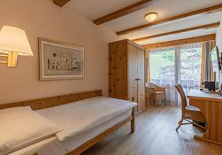 Chambre simple Classic à l'Sunstar Hotel Grindelwald avec lit simple, armoire en bois, coin salon près de la fenêtre et balcon avec vue sur les montagnes