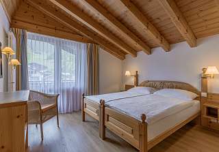 Espace nuit de la Chambre familiale Village au Sunstar Grindelwald avec lit double sous un plafond à poutres en bois