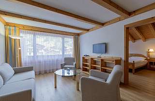 Wohnbereich eines Familienzimmers Dorf im Sunstar Hotel Grindelwald mit Sitzecke, Fernseher und Blick ins angrenzende Schlafzimmer