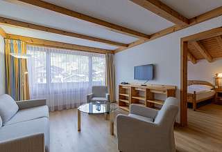 Wohnbereich eines Familienzimmers Dorf im Sunstar Hotel Grindelwald mit Sitzecke, Fernseher und Blick ins angrenzende Schlafzimmer