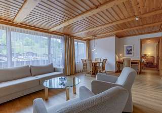 Espace salon de la Suite First au Sunstar Grindelwald avec coin salon, table à manger et vue sur le village