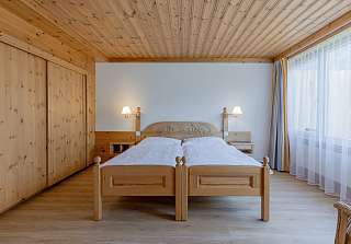 Espace nuit de la Suite Junior au Sunstar Grindelwald avec lit double et lambris en bois